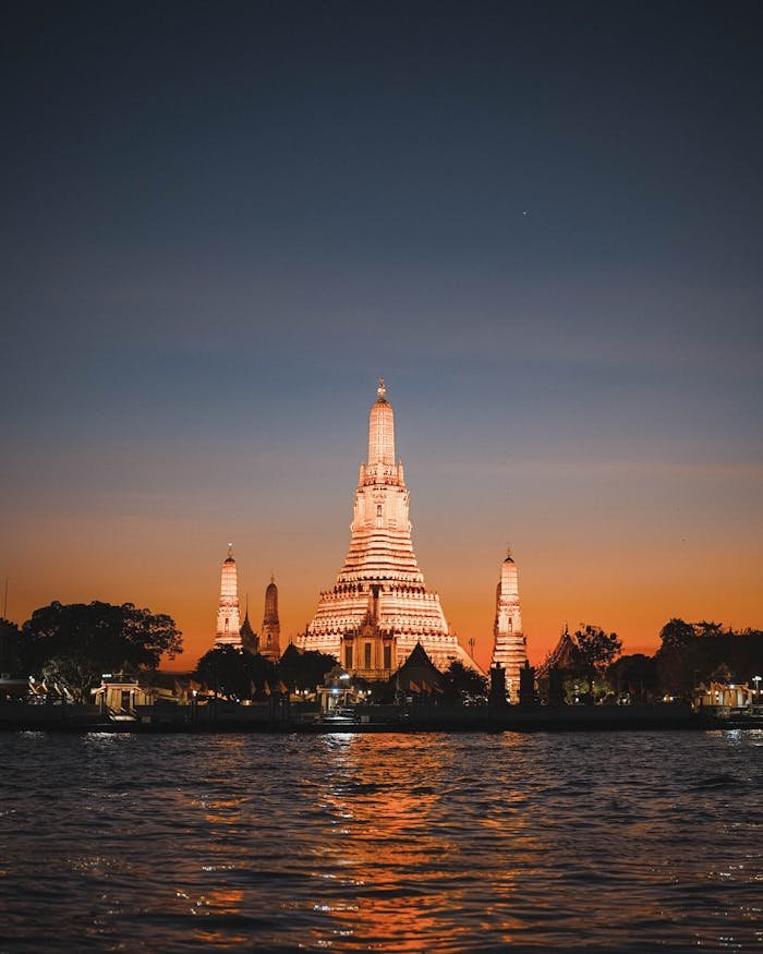 Beautiful view of Wat Arun temple illuminated during sunset along the Chao Phraya River in Bangkok, Thailand.