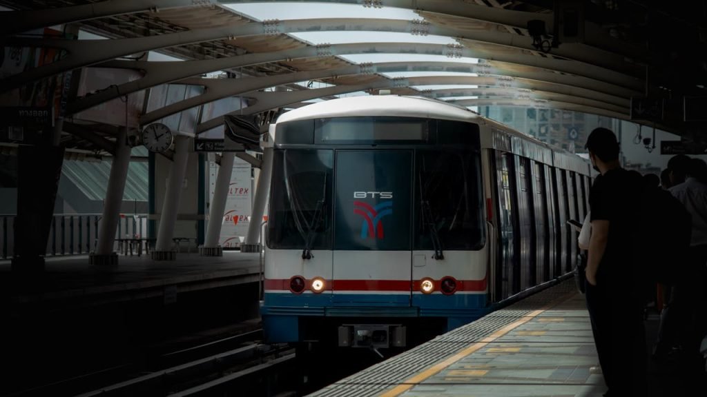 Bangkok Skytrain arrives at urban metro station platform with people waiting, showcasing city transportation.