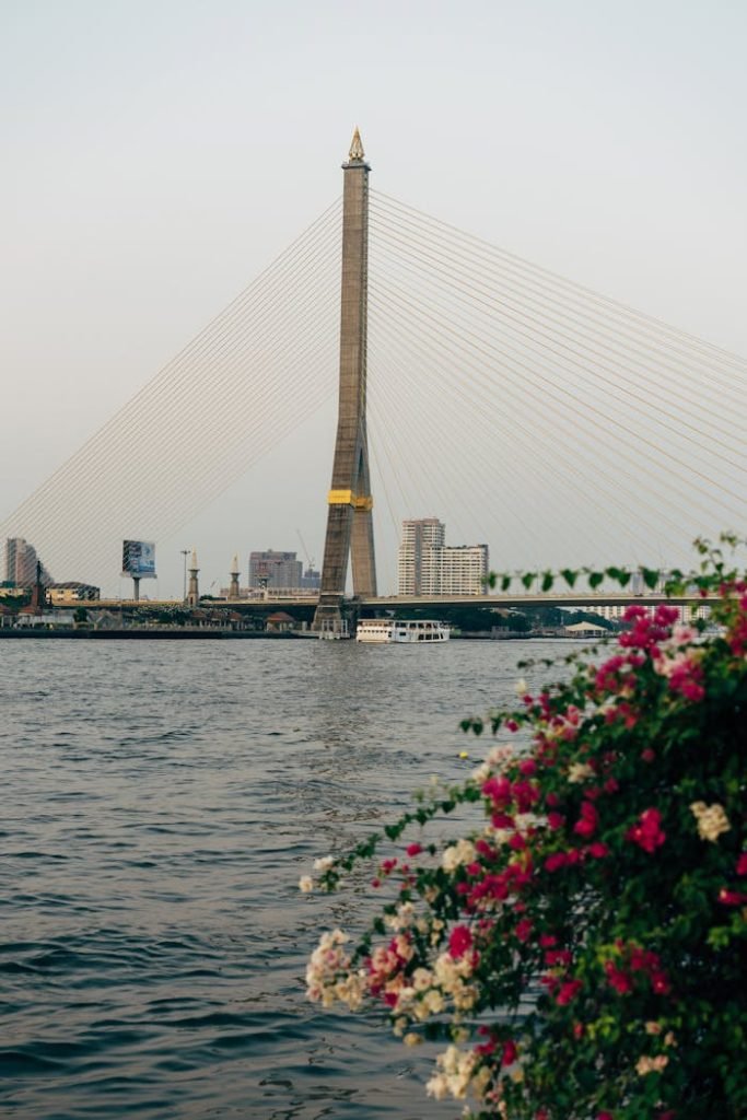 Stunning view of Rama VIII Bridge in Bangkok with vibrant flowers in the foreground, over Chao Phraya River.