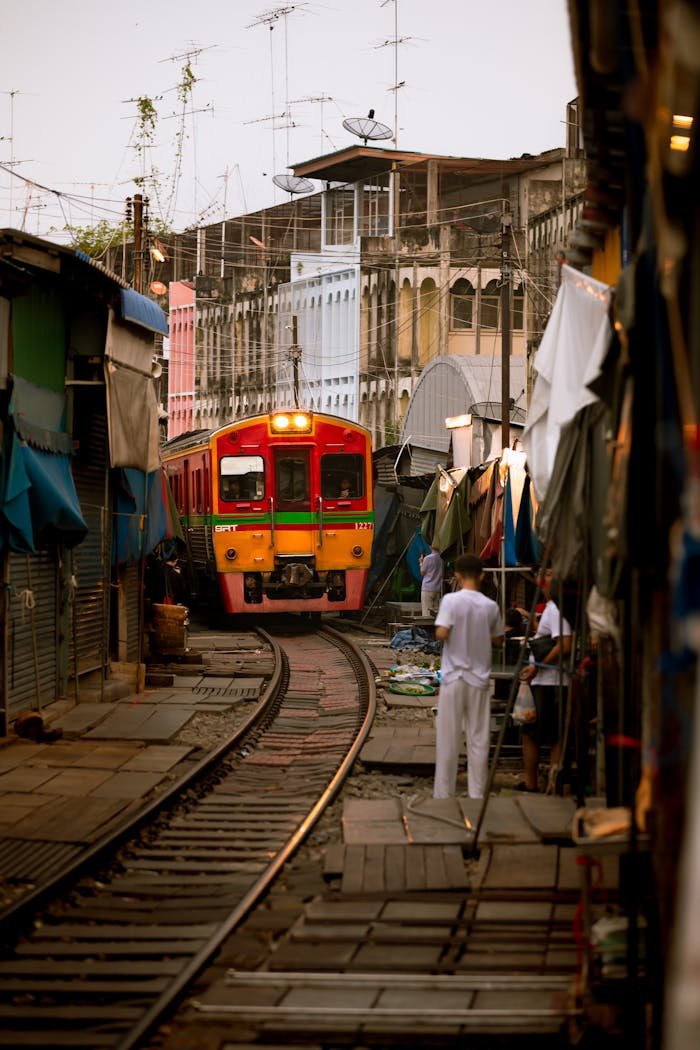 A colorful train traverses through a bustling Bangkok market, surrounded by local vendors.